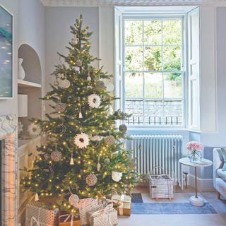 A living room with a fireplace and a decorated lit-up Christmas tree in the corner with presents underneath