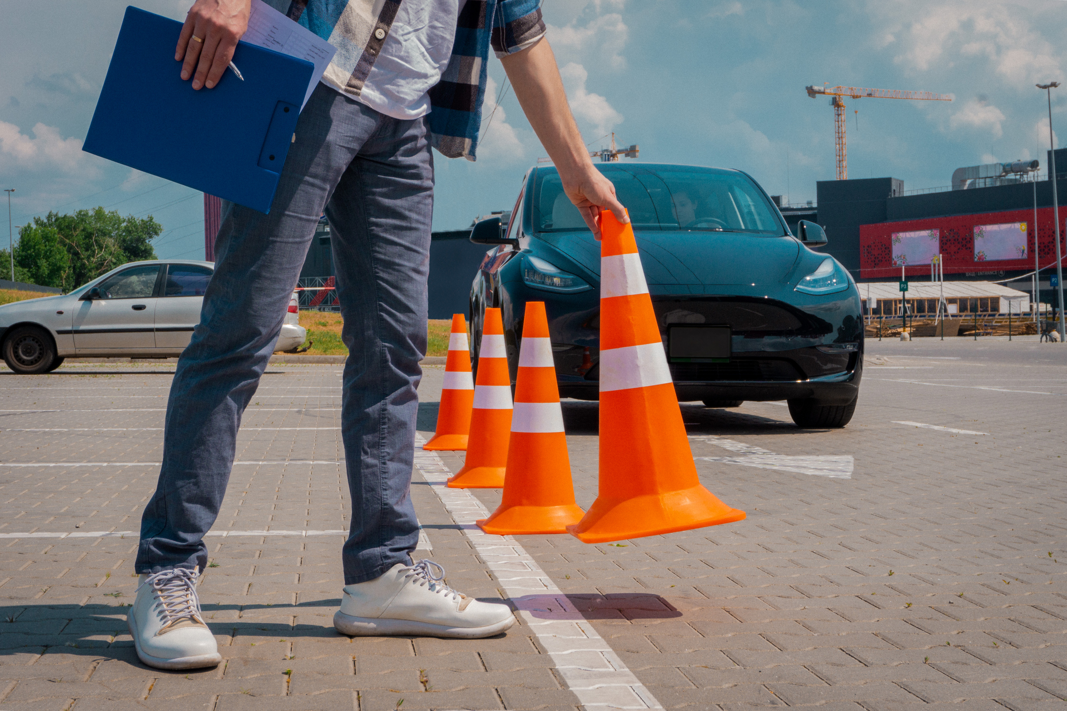 Male driving instructor standing with orange traffic cones and clipboard in his hands during exam outdoors. 