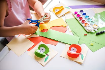 Little girl cutting colorful paper at the table