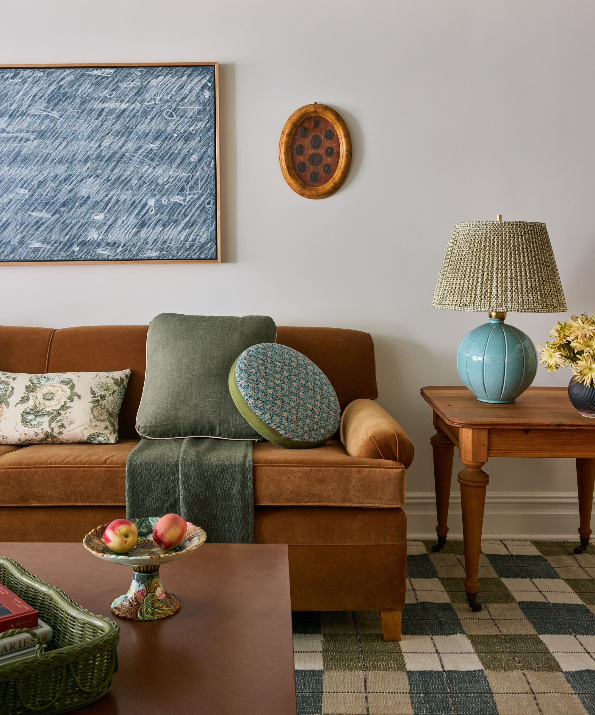 Living room with caramel sofa, layered green pillows, patterned textiles, blue lamp and antique wood side table.
