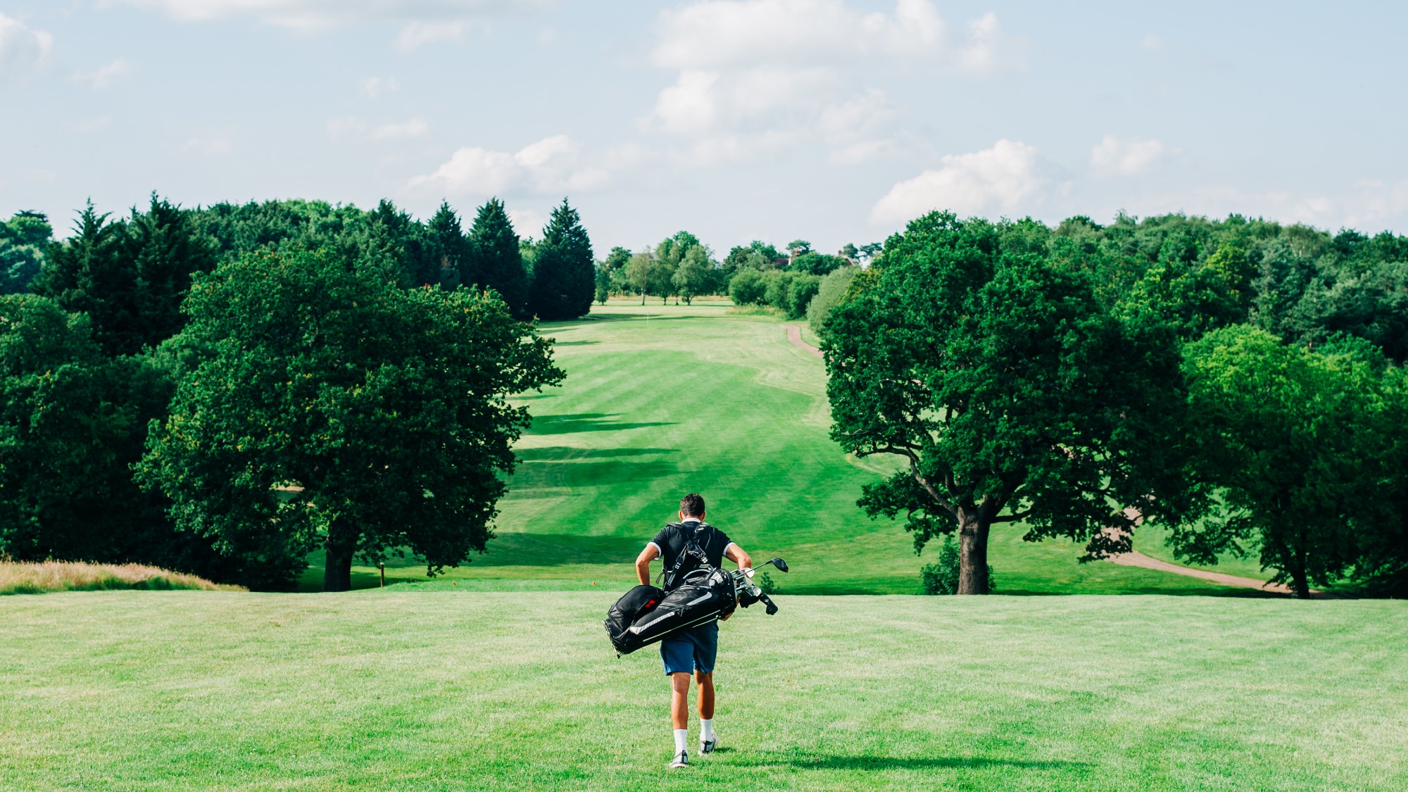 A rear view of a golfer walking down a fairway