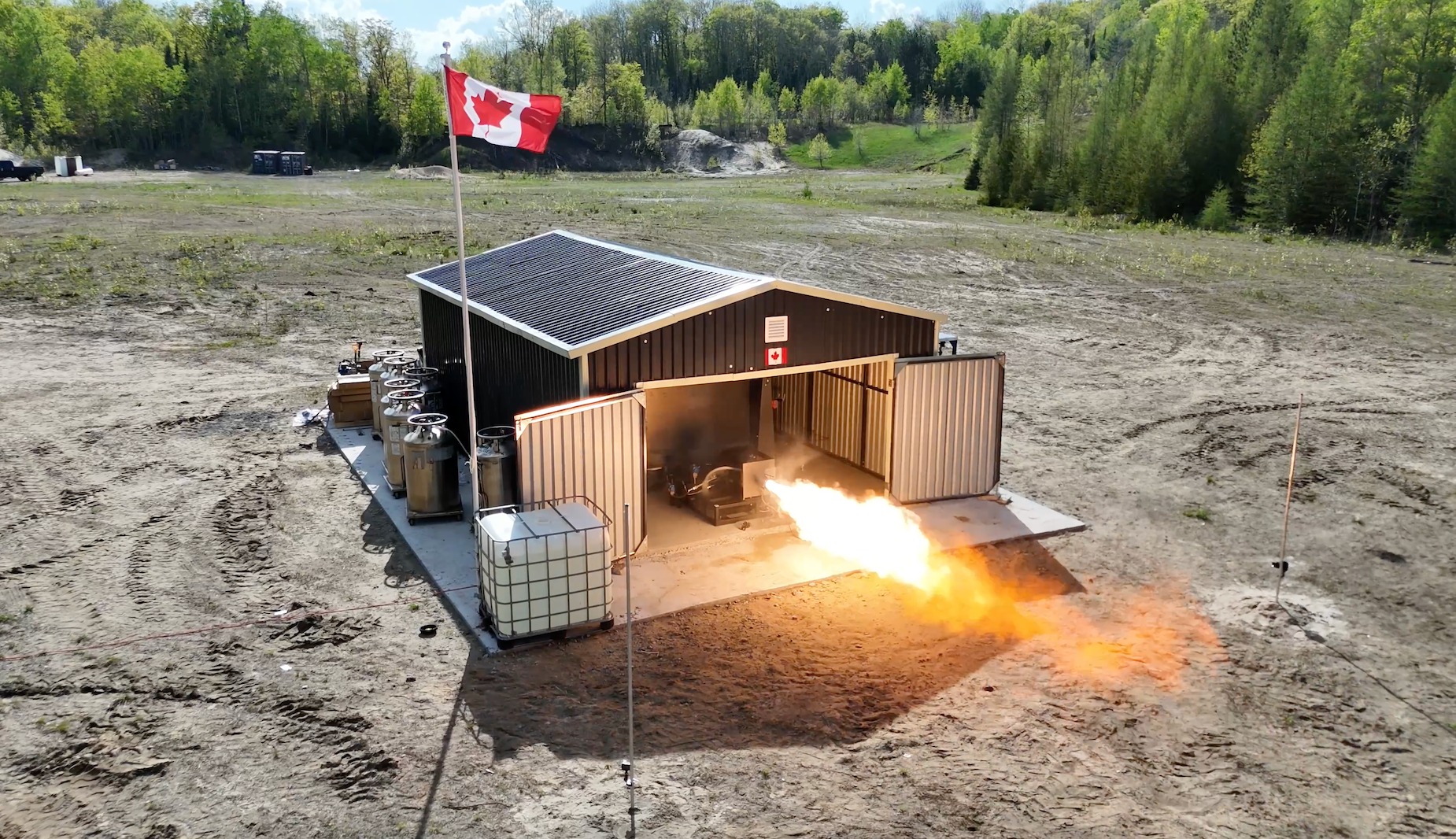 A large shed with doors swung open spews hot fire from a rocket engine from within.