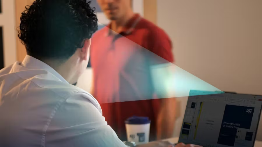 A man sitting at a laptop with a beam-like overlay illustrating an invisible sensor field, detecting another person standing behind him.