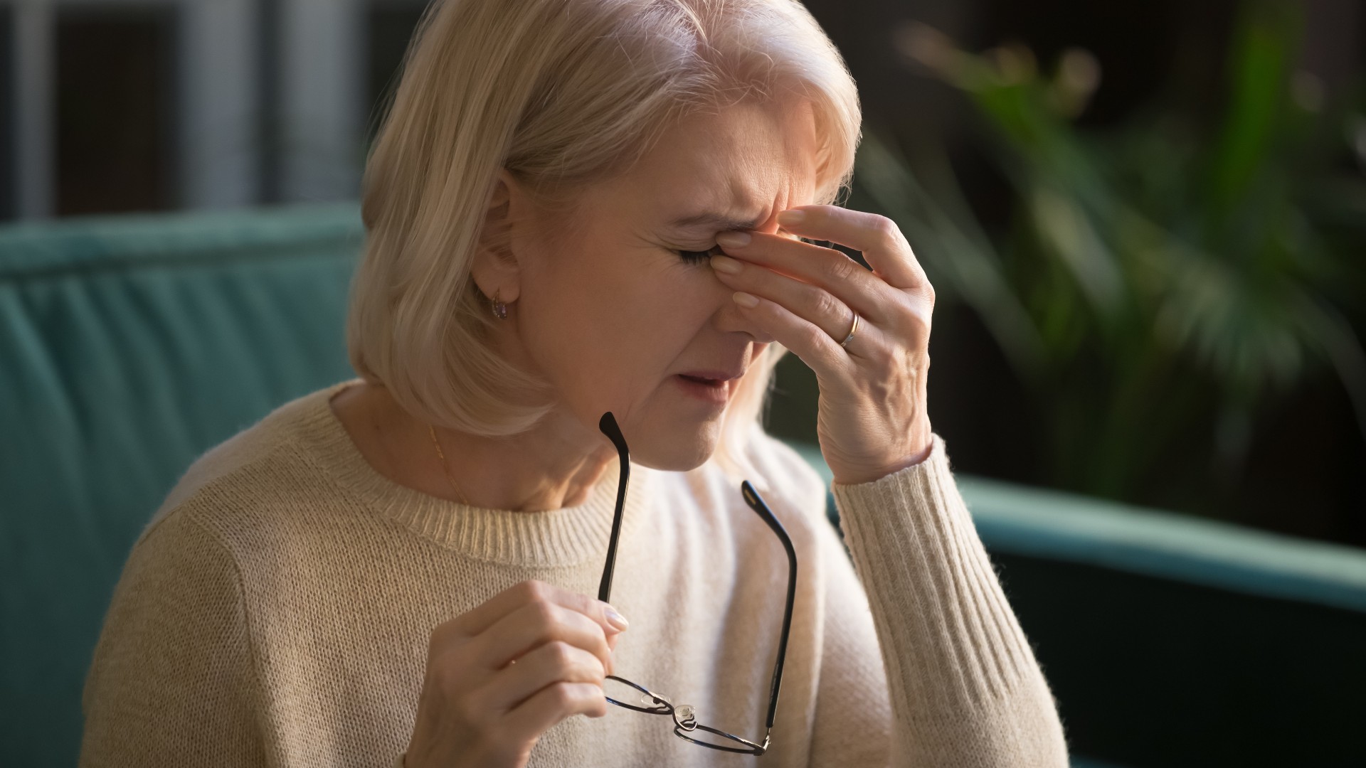 Anciana quitándose las gafas y frotándose los ojos o con dolor de cabeza_fizkes a través de Shutterstock