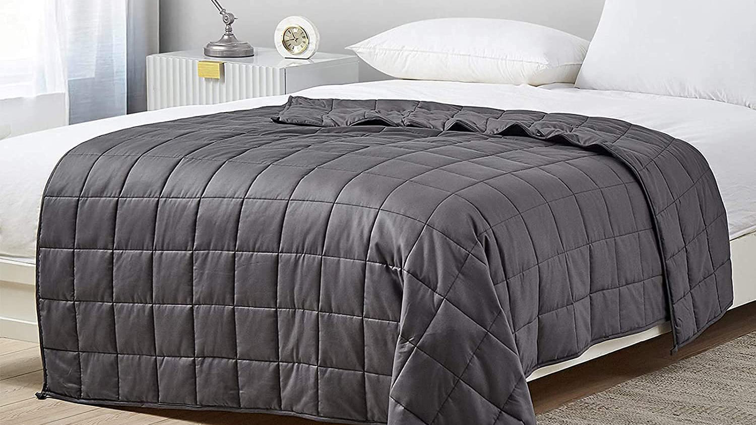 The YNM Weighted Blanket in gray placed on a white duvet