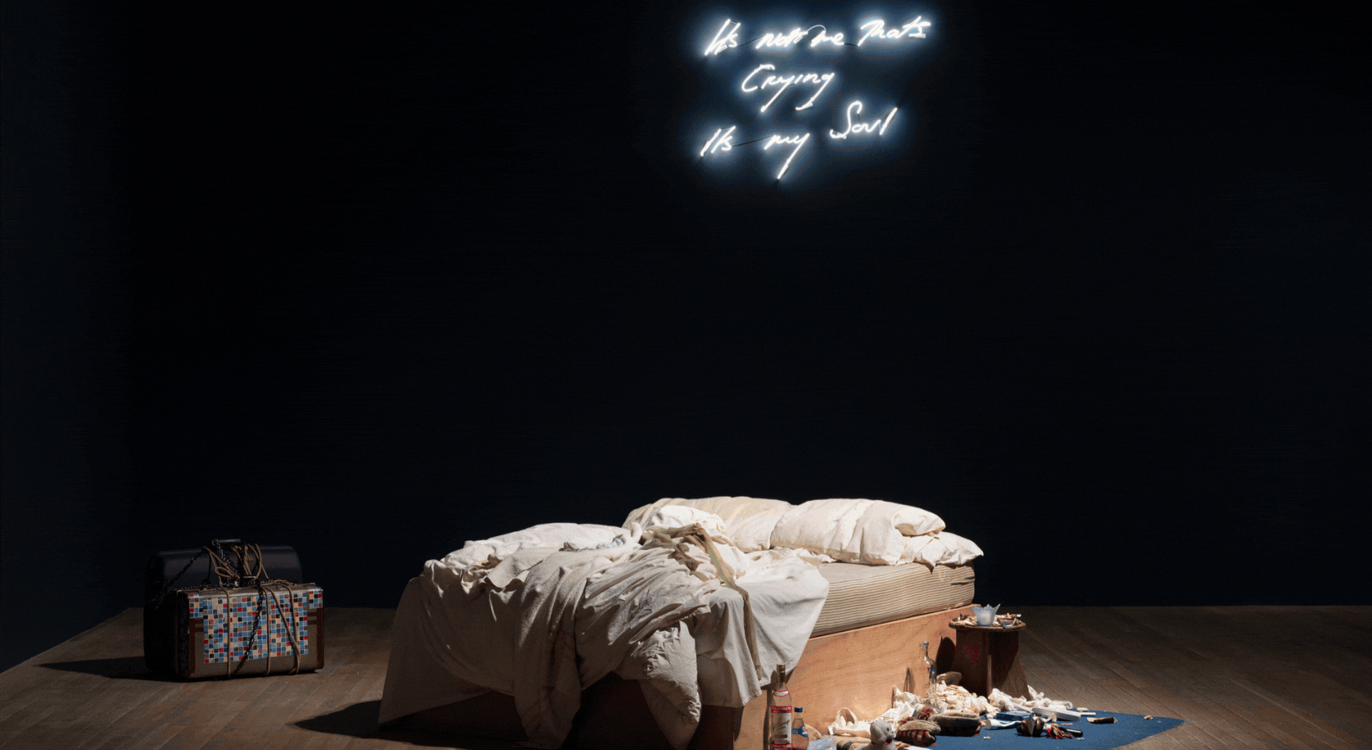 A rotating gif showcasing a multidisciplinary exhibition of paintings, furniture installations, framed nude self-portraits, quilted textiles with colorful slogans, and more.