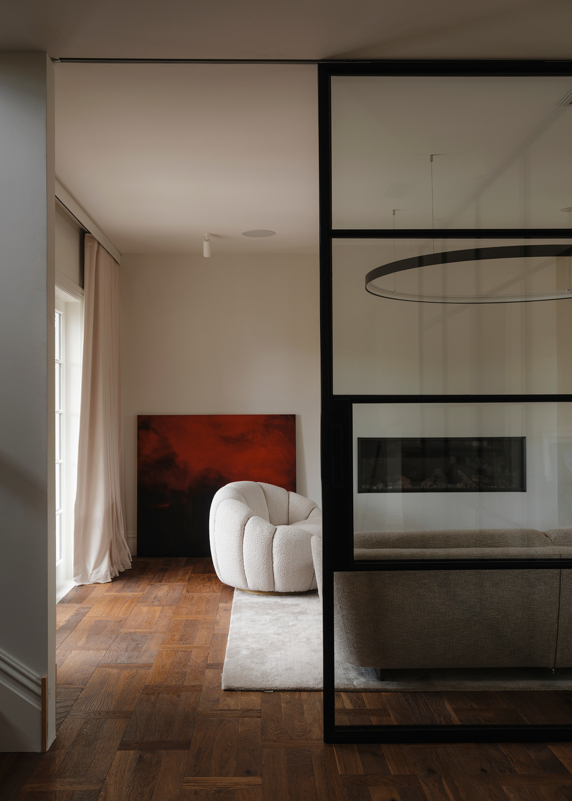 A living room with wood floors, white walls, a large rug, beige furniture and a red painting