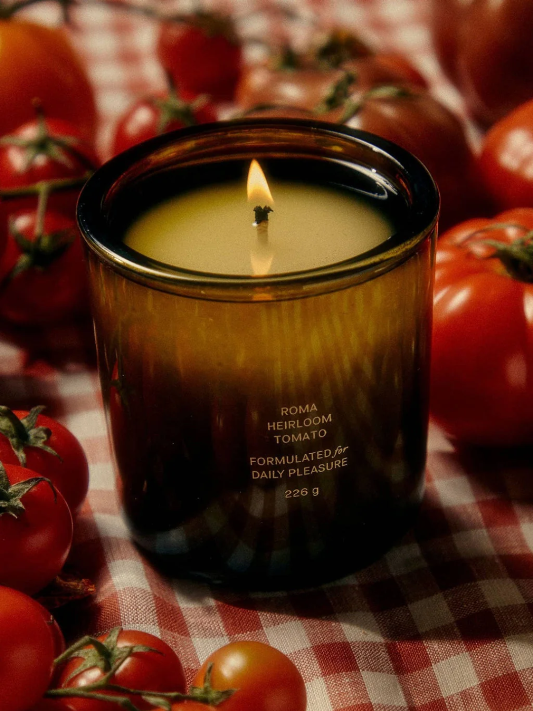 A green glass candle from Flamingo Estate surrounded by heirloom and cherry tomatoes