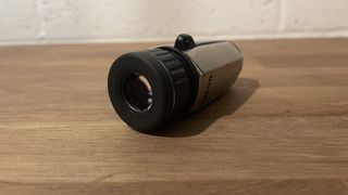 A monocular laying on a wooden shelf.