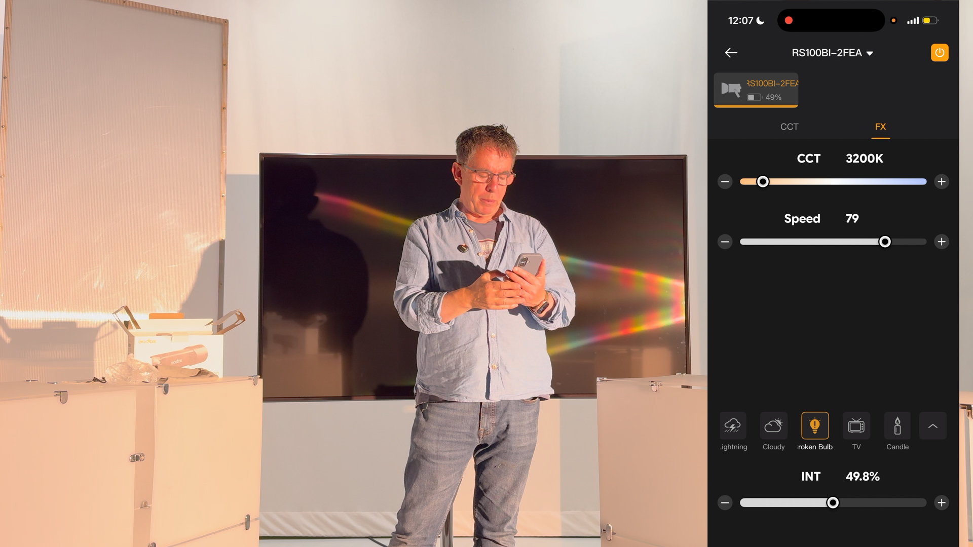 Shot of the reviewer being illuminated by the RS100Bi and controlling the LED via his phone. An insert of the Godox App shows adjustable properties for the Broken Bulb effect such as Speed.