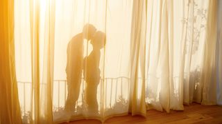 Shadow of romantic couple behind curtain in bedroom