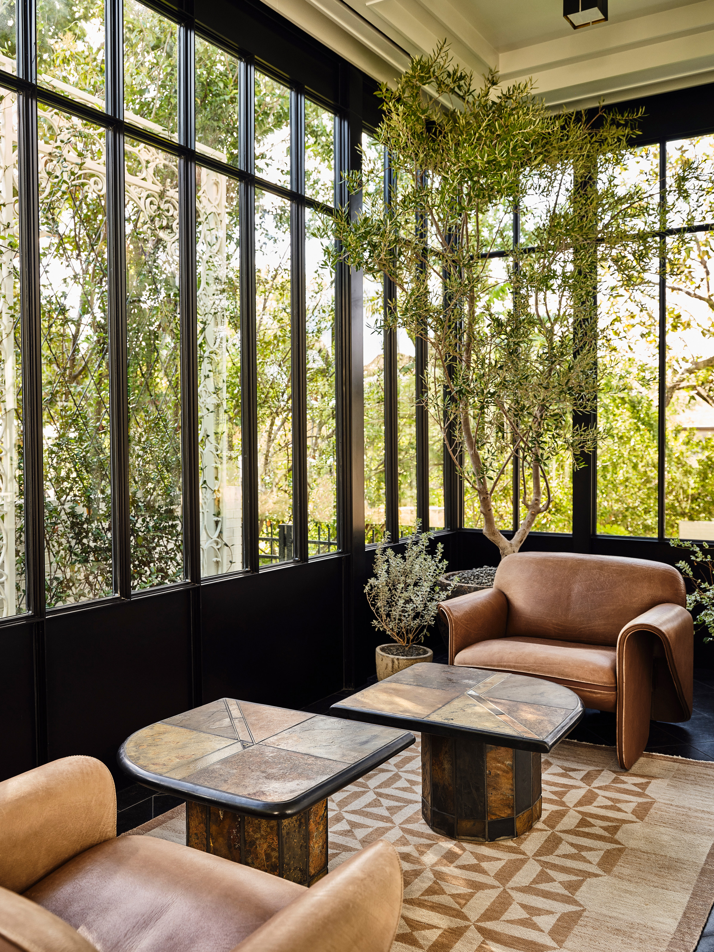 Conservatory or sunroom with black framed windows, tan leather armchairs, curved coffee tables and beige patterned rug