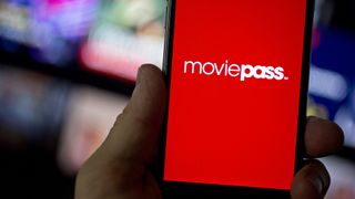 A hand holds a phone bearing the original MoviePass logo