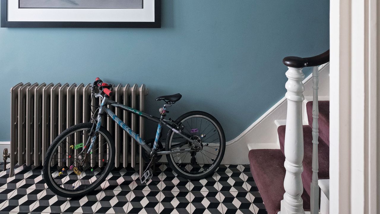 Hallway with geometric black and white floor tiles, large metal radiator, stairway and original cornice