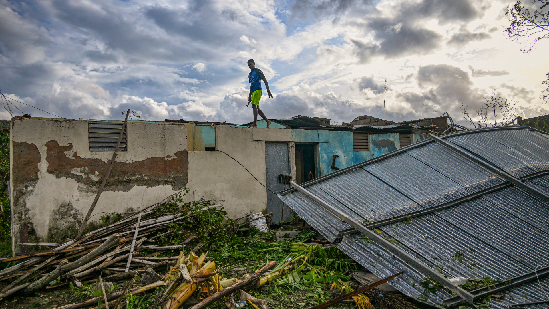 A resident of the town of El Cobre, in the province of Santiago de Cuba, walks on the roof of his damaged home after the passage of Hurricane Melissa, on October 29, 2025. Hurricane Melissa was moving towards Bermuda on Thursday after ripping a path of destruction through the Caribbean that left at least 20 people dead in Haiti, and parts of Jamaica and Cuba in ruins.