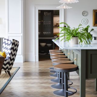 kitchen dining/living space with island with bar stools, parquet flooring, rug, armchair on left, fluted pendant lights, pantry at rear