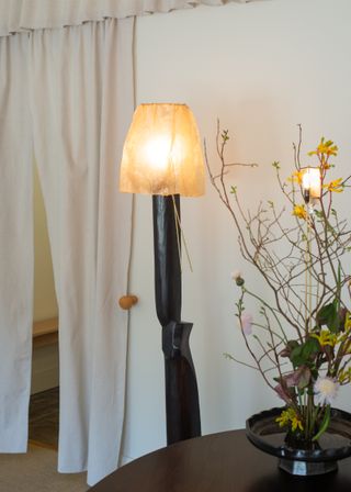 A lamp with black stem and yellow shade, and an ikebana arrangement in a vase on the table