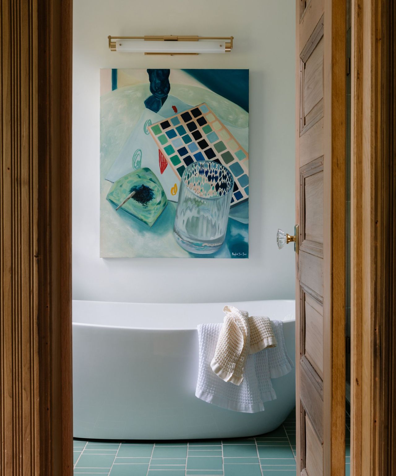 A brownstone bathroom with a standalone bathtub, wooden door, and piece of blue and green artwork