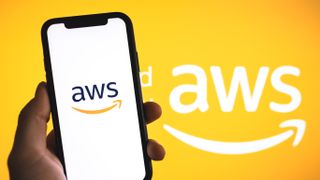 A hand holding a phone with the AWS logo in front of the AWS logo on an orange background