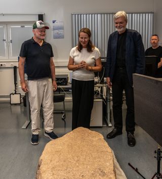 Three people stand and look at a large stone