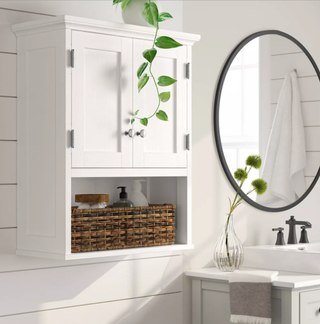 white bathroom cabinet next to a black mirror with a plant on top