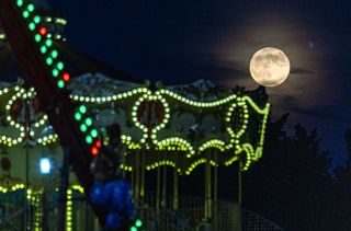 A yellow sphere in the sky over carnival rides illuminated with green lights