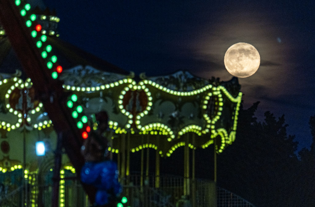 A yellow sphere in the sky above amusement rides illuminated with green lights