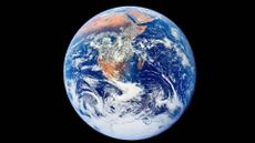 A blue and white sphere with brown continents on it is seen in the darkness of space.
