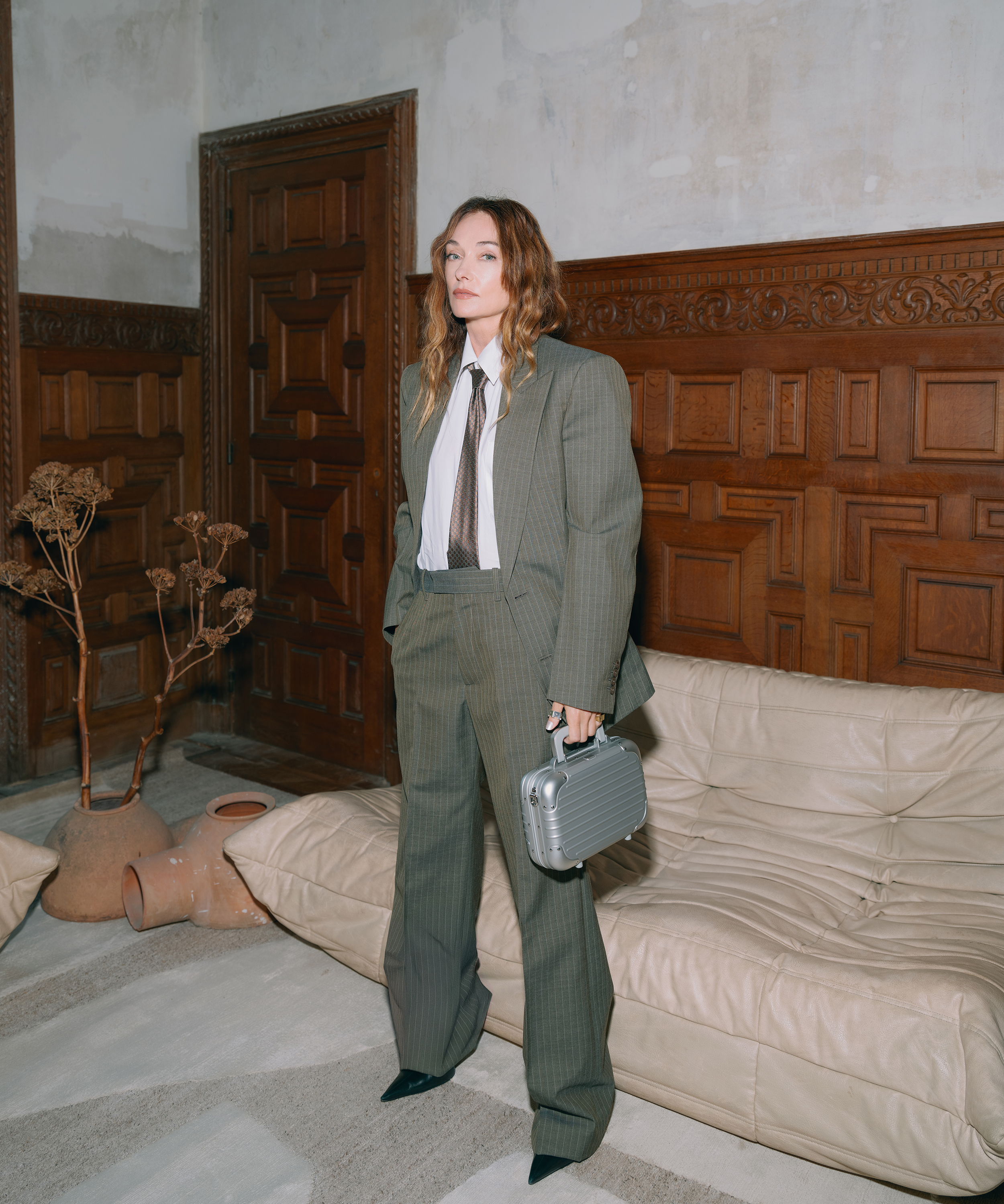 Kelly Wearstler stands in a grey suit and tie in front of a Togo sofa