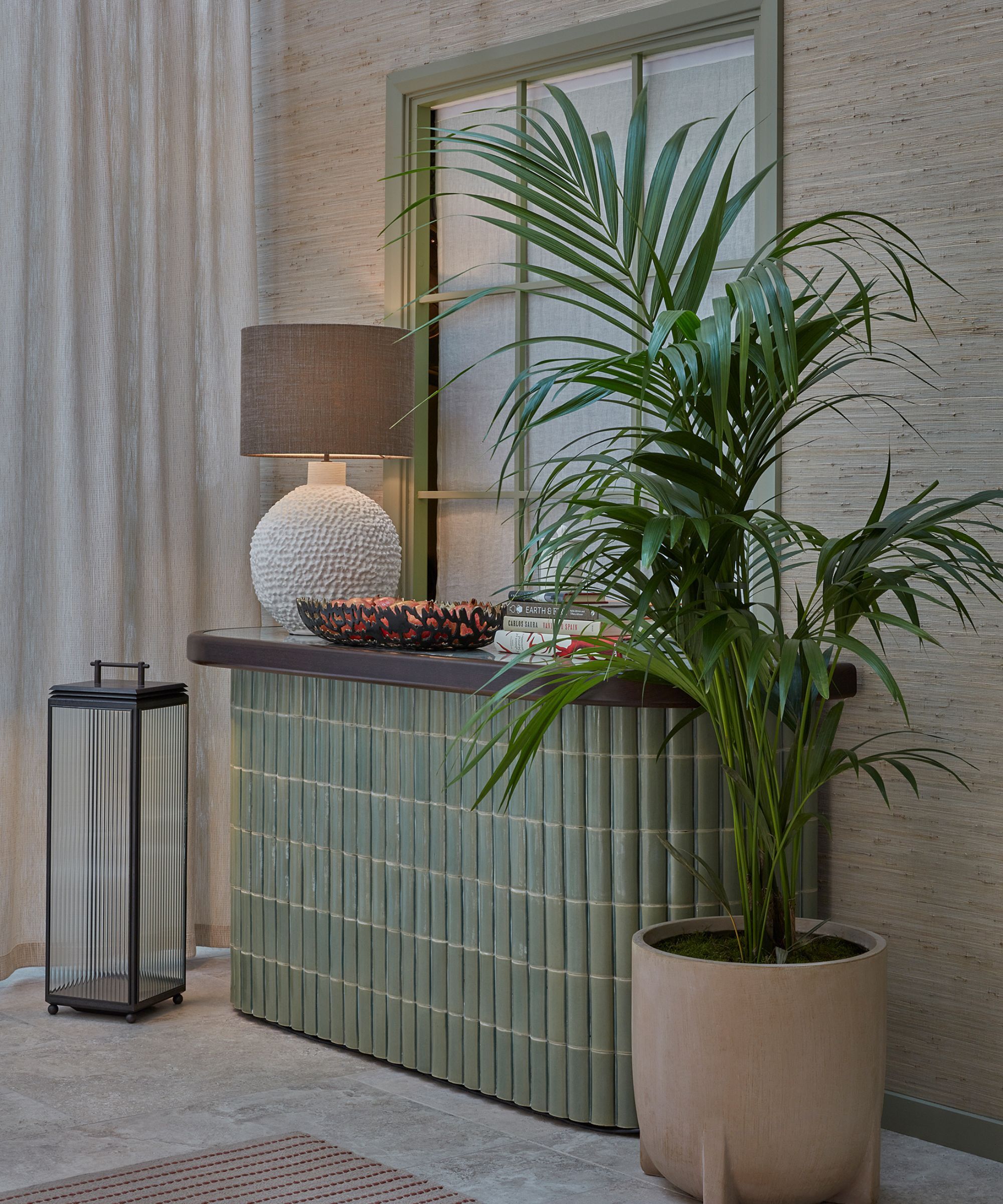 A corner of a courtyard garden with tiled sideboard with a lamp, decorative items and potted plant