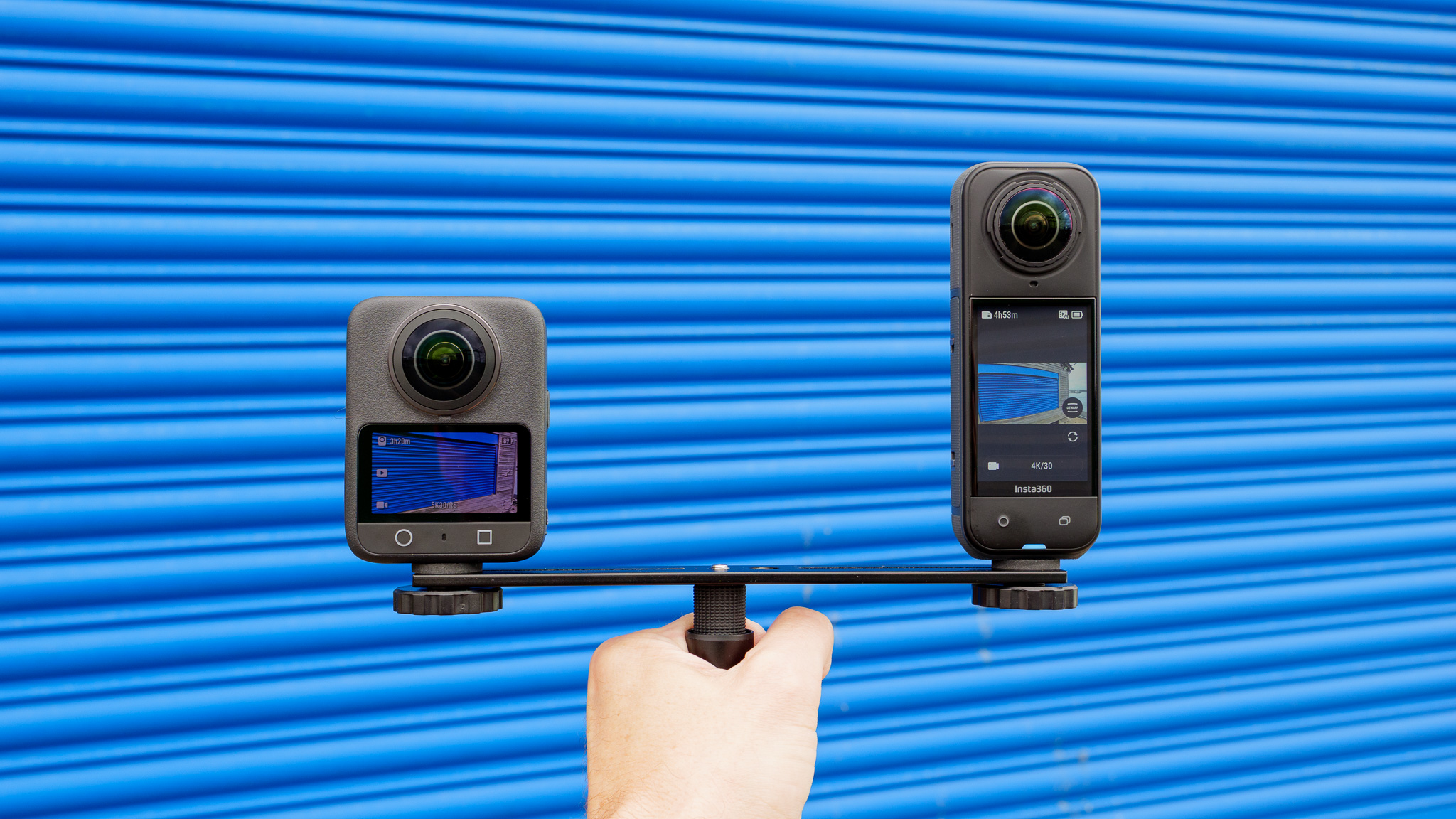 DJI Osmo 360 and Insta360 X5 cameras mounted on dual camera rig against blue background