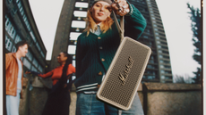 A young woman in an urban area dangles the Marshall Middleton II speaker from its carrying strap
