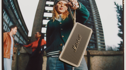 A young woman in an urban area dangles the Marshall Middleton II speaker from its carrying strap