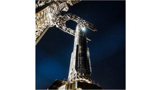 closeup of a big silver rocket on a launch pad at night.