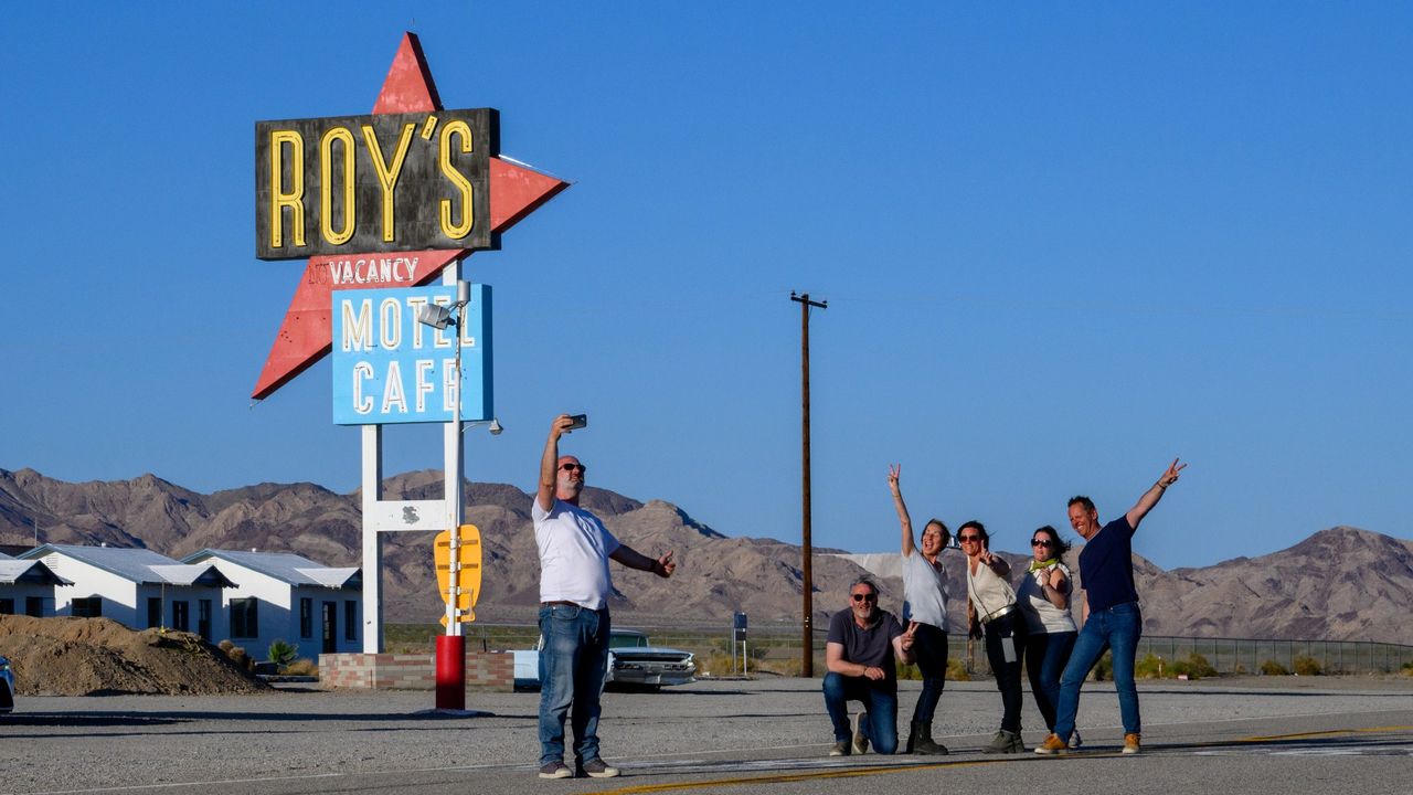 A group of tourists pose in front of the space-age Roy&#039;s sign in Amboy, California