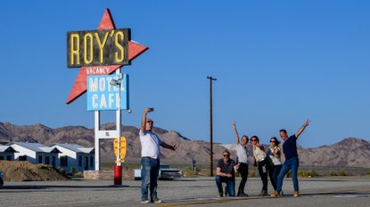 A group of tourists pose in front of the space-age Roy's sign in Amboy, California