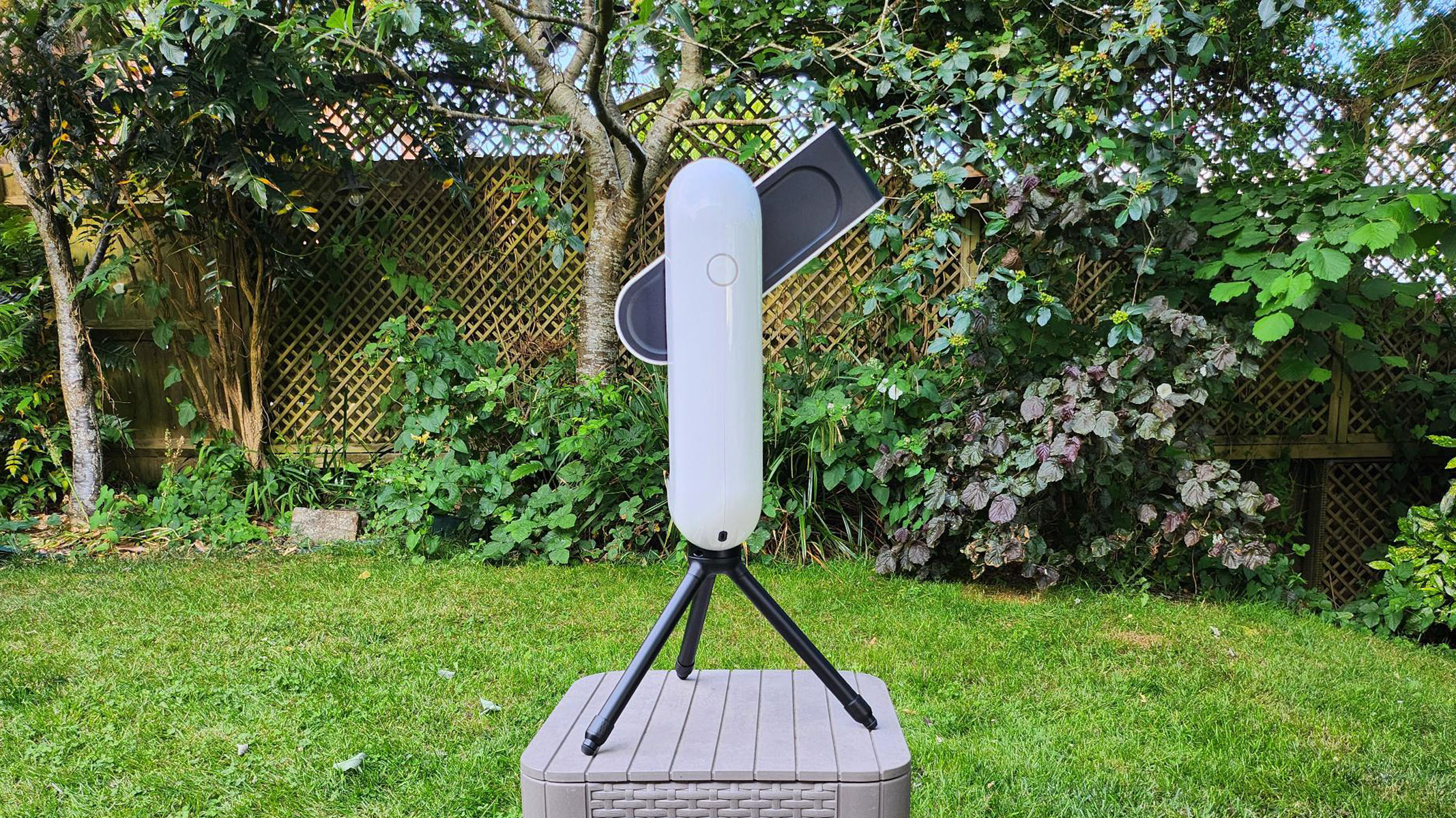 The Vaonis Vespera Pro pointed upwards with the power button visible with trees and grass in the background.