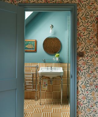 colors experts say to avoid in 2024, teal and yellow bathroom, matching floor and wall tiles, teal painted upper wall and woodwork, towel rail, basin, artwork, mirror, wall light