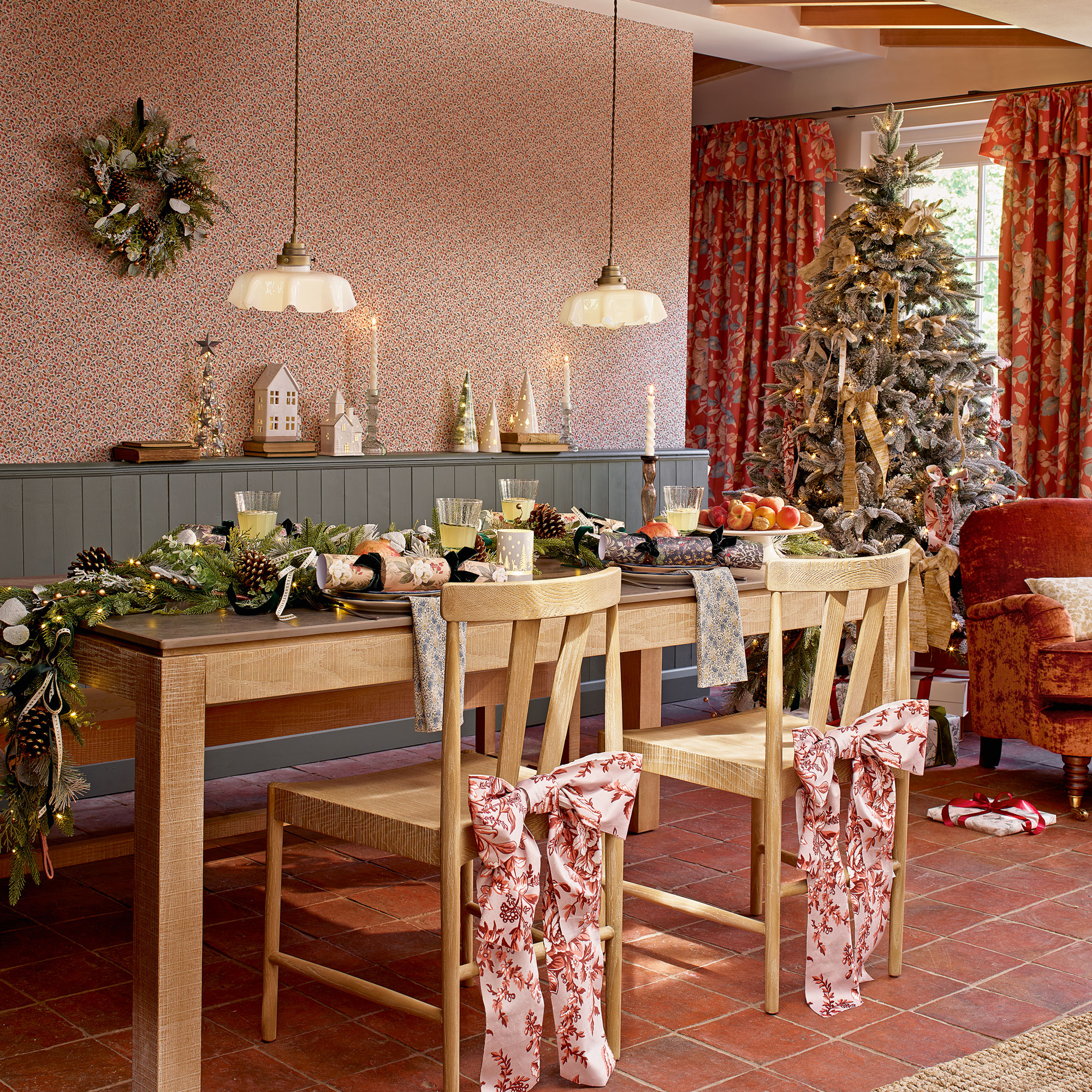 Dining room with pinky ditsy wallpaper, blue wall panelling, an oak table with matching chairs, frilly lights over the table and a Christmas tree in the background