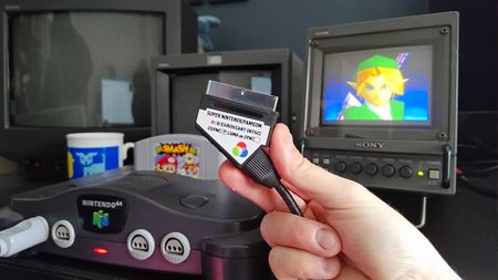 Hand holding RGB SCART by Retro Gaming Cables next to N64 connected to 6-inch Sony Trinitron PVM CRT with Link from Super Smash Bros opening on screen.