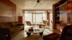 View into a modern living space with an olive green sofa and deep red armchair around a wooden coffee table. Another two armchairs are facing the view out of the floor to ceiling windows.