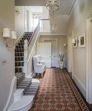 Traditional hallway with tiled floor, white painted walls, striped stair runner, bench near stairs, glass pendant lights