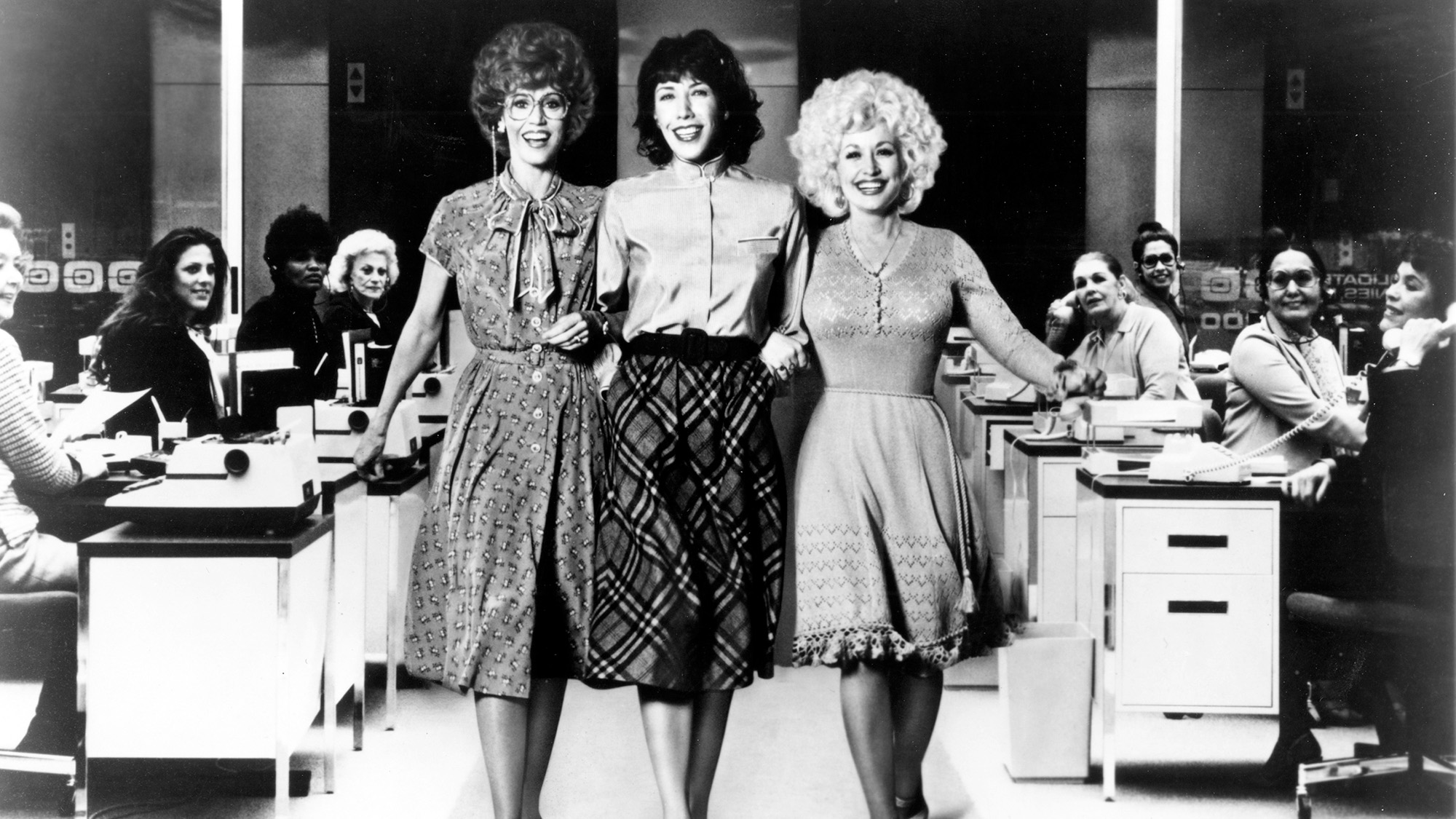 Jane Fonda, Dolly Parton, And Lily Tomlin skipping in the office in 9 to 5. 