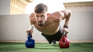 Man outdoors doing a push-up with two kettlebells 
