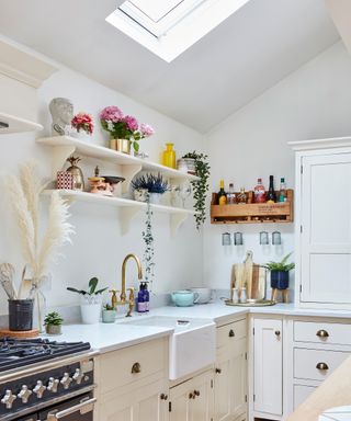 Pretty white kitchen with open shelving styled with houseplants, flowers, and decorative treasures.
