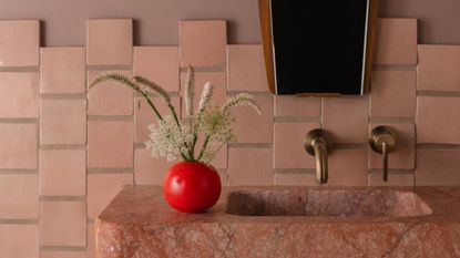 bathroom counter with terracotta tiles, mirror with timber detailing, red marble sink, and bright red vase