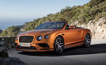 Orange Continental Supersports Bentley parked near the edge of the mountain road. We see trees and a sea behind the car.