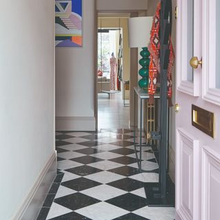 A narrow hallway with a pink front door and a chequered marble floor