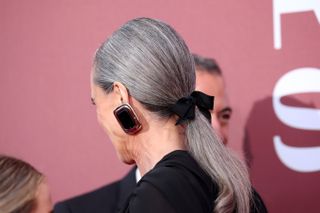 Andie MacDowell wears her grey hair in a neat low ponytail and secured with a black bow