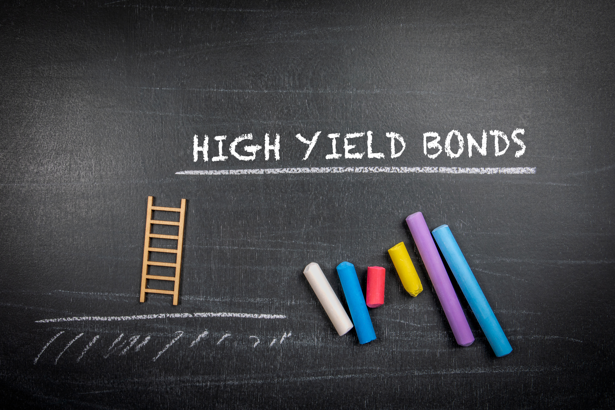 High yield bonds. Text and colored pieces of chalk on a dark board.